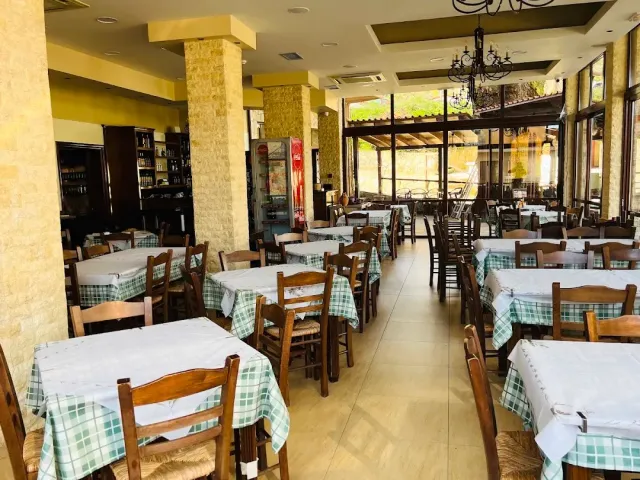 A large hall with green checked tablecloths, wooden chairs, stone columns and a chandelier