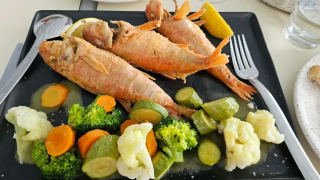Two fried red fish on a black tray beside steamed vegetables