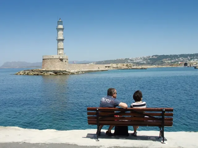 A stone lighthouse at the end of the breakwater, with two people sitting on a bench facing it