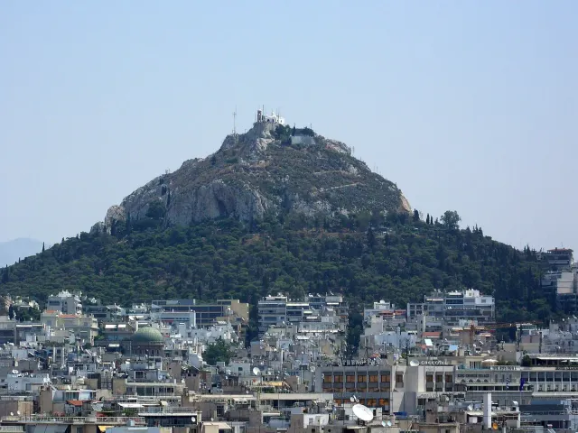 A pointed pine covered hill rising above the city rooftops
