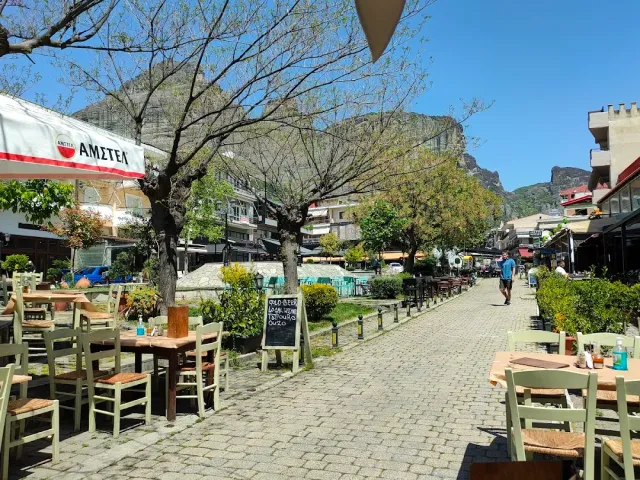 A paved street with wooden tables and chairs on both sides and rock cliffs in the background