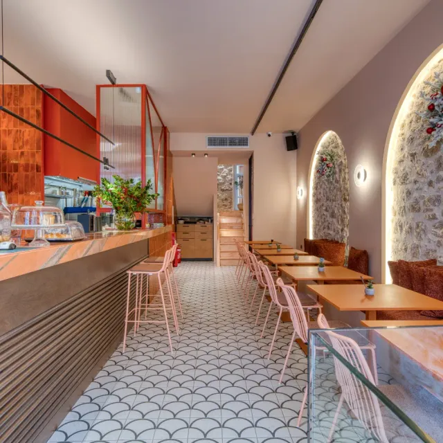 A narrow space with a counter, pink stools and a patterned tiled floor