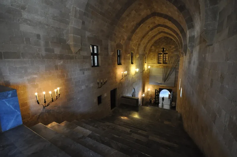 A vaulted stone hall lit by candelabra with wide steps at its end