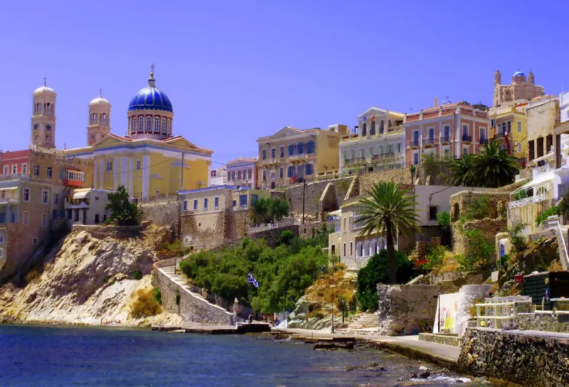 Colourful neoclassical mansions above the sea beside a church with a blue dome and two bell towers