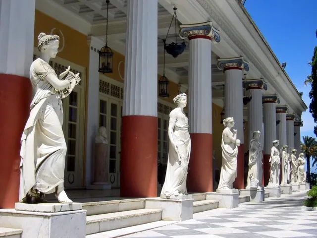 A terrace with a row of marble statues between columns, above a garden