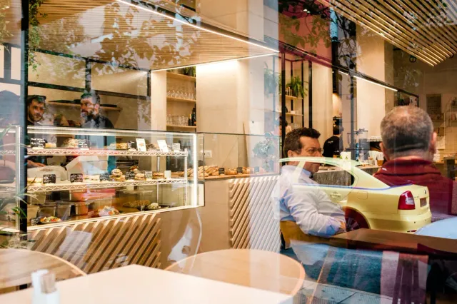A view through a glass window to a pastry case and seated people, with street reflections