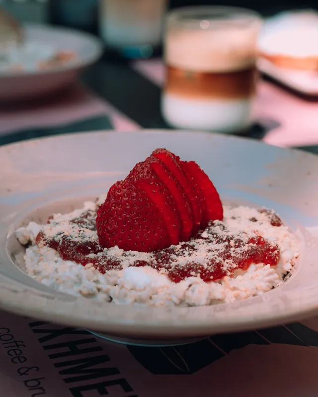 A bowl of white cheese with jam and sliced strawberries, and a glass of coffee behind