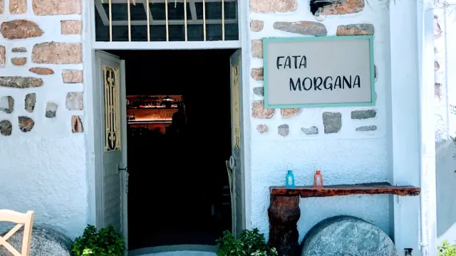 A dark entrance in a whitewashed stone wall, a small sign beside it and bottles on a wooden ledge