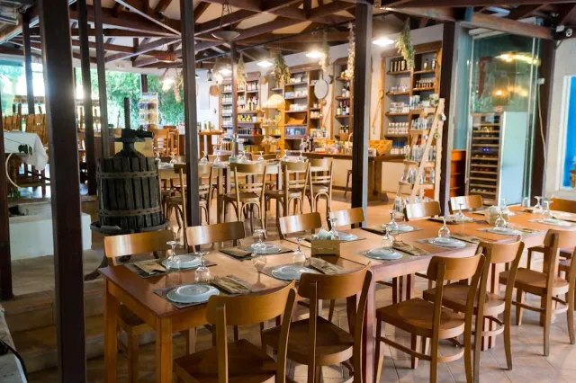 A hall with wooden beams, long laid tables, shelves of jars and an old wine press