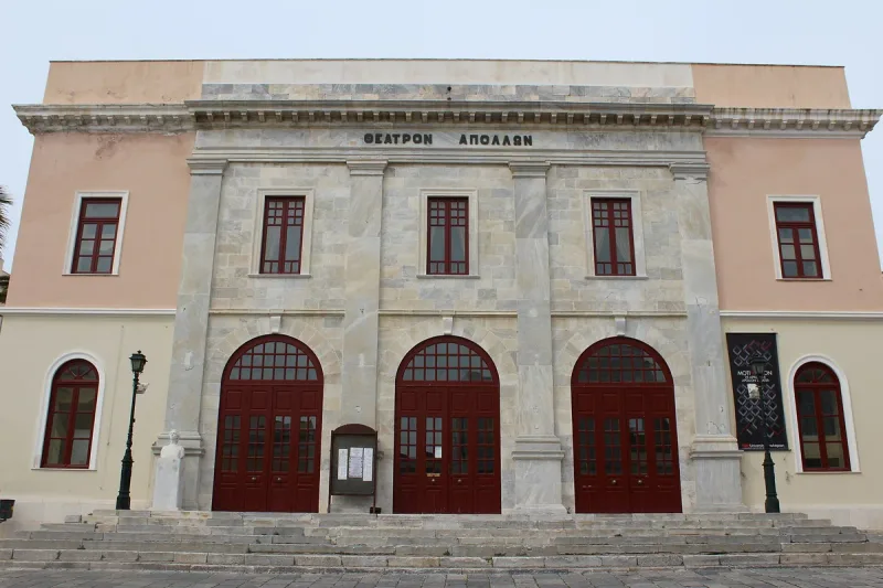 A pink neoclassical facade with three arched red doors