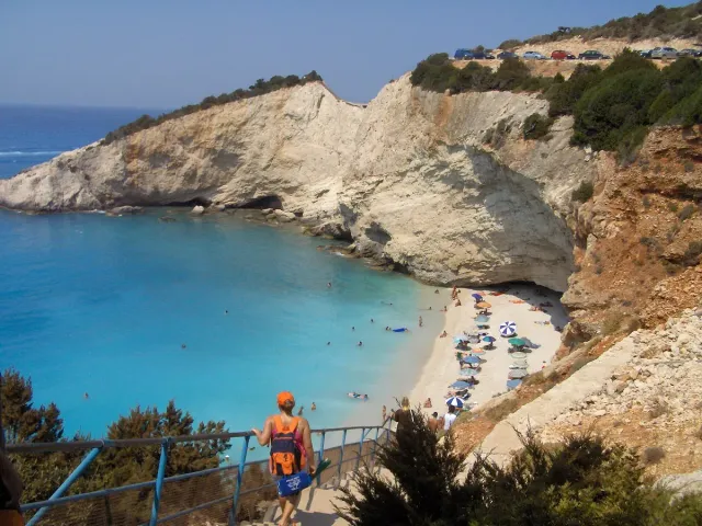 A pebble beach at the foot of a steep white cliff, facing turquoise water
