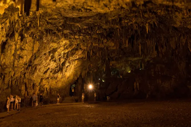 A cave chamber with stalactites and stalagmites in warm lighting