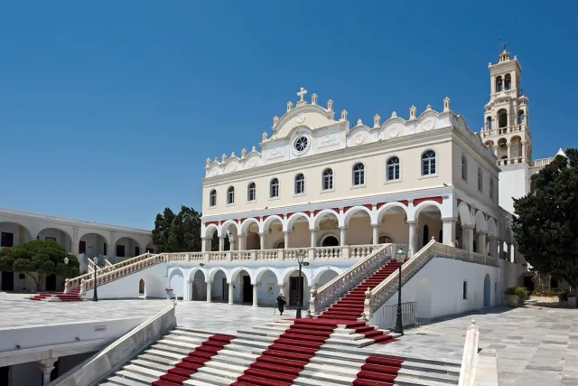 A white church with arches and a bell tower, a red carpet running up the steps