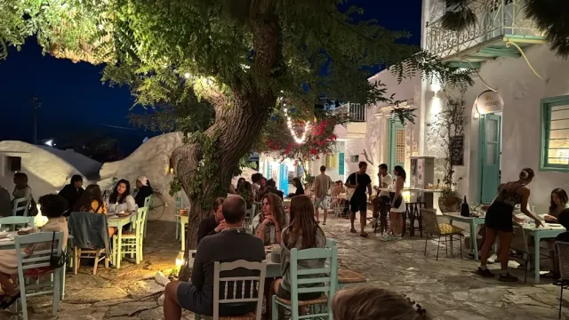 A village square at night with a large tree, turquoise chairs and many diners