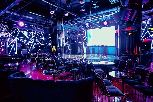 A dark club hall with neon lighting, an illuminated stage and dark velvet sofas