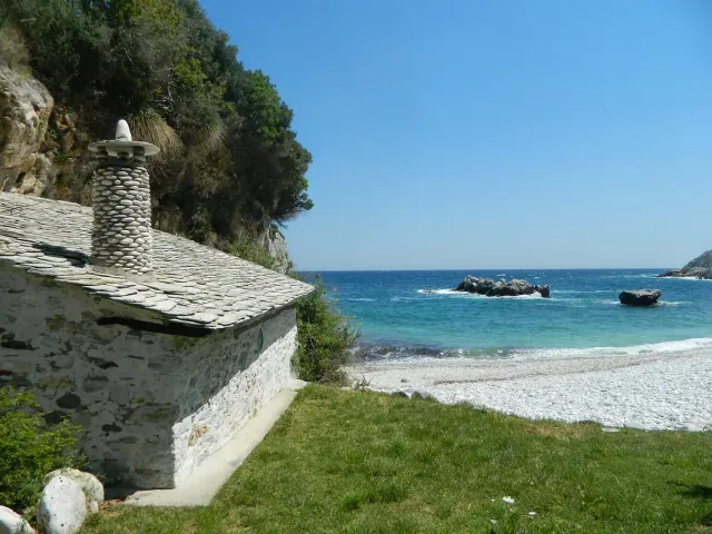 A stone house on a pebble shore in a small bay, with rocks in the sea