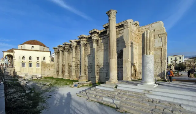 A row of standing marble columns beside an ancient stone wall in the middle of the city