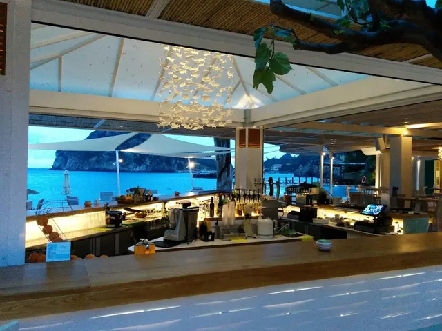 A white bar counter in twilight, with a bay surrounded by green cliffs behind it