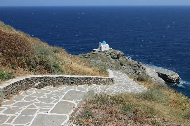 A small white church on a flat rock in the sea, with a stone path leading down to it