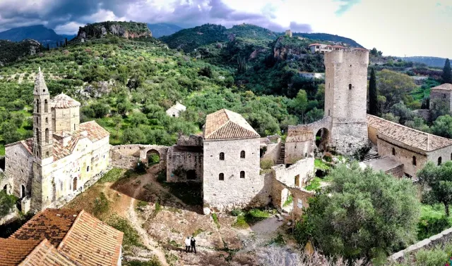 A stone village with a square tower and a church, tiled roofs and green hills around