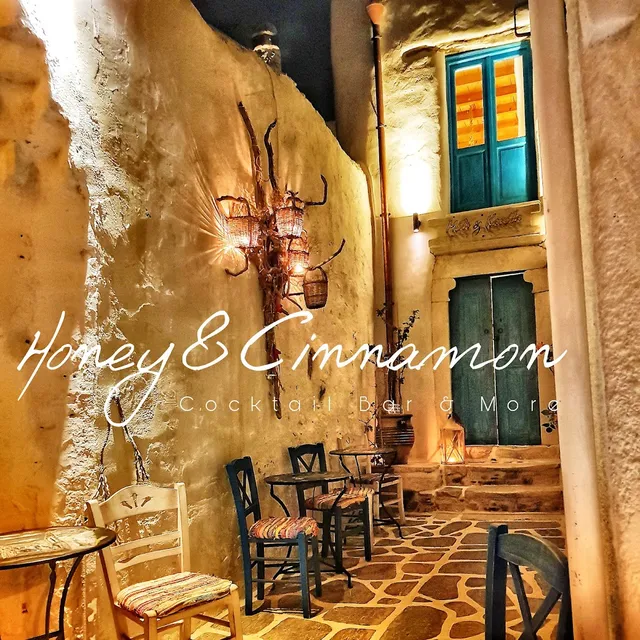 A paved alley between whitewashed walls, with painted wooden chairs and glowing wicker lamps