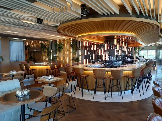 A round bar with an arched wooden ceiling, high bar stools and tables around it