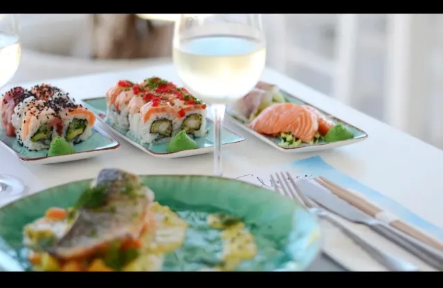 Trays of sushi and sashimi beside a glass of white wine on a light table
