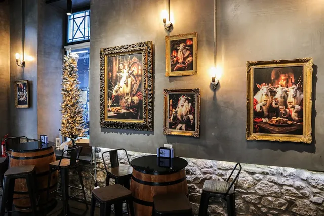 Wooden barrels as tables against a grey wall with paintings of goats in gilded frames