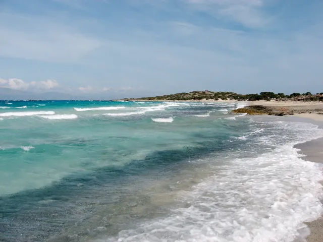 Shallow turquoise water and waves on a white sand shore, with a low scrub covered island