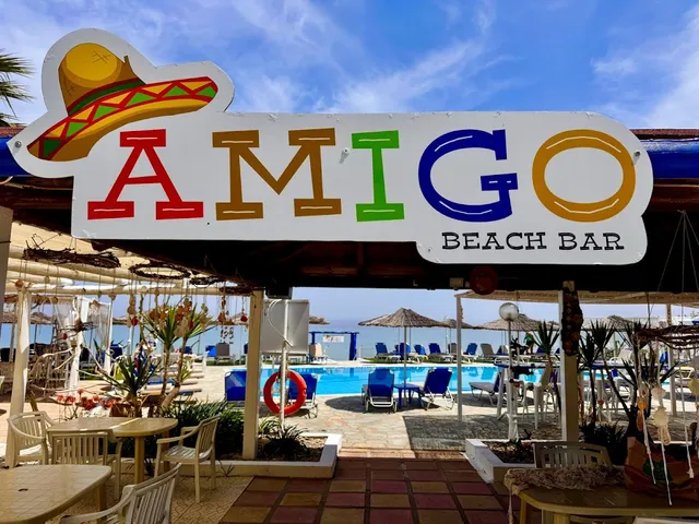 A colorful sign with a sombrero above an entrance, with a pool and blue sun loungers behind it