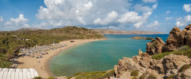 A curved bay with a sandy beach, rows of parasols and green blue water