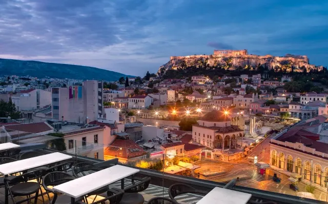 White tables on a roof, facing the city rooftops and a lit rock hill at dusk
