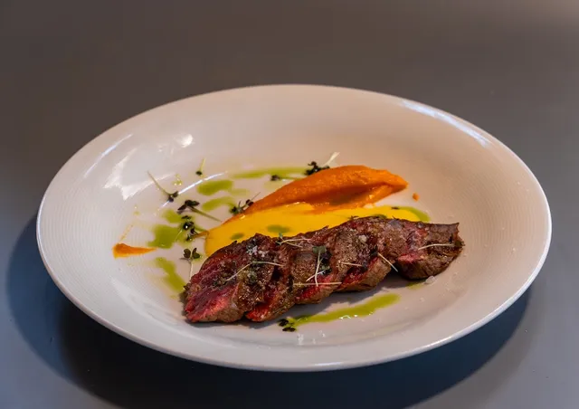 A grilled cut of meat on orange and yellow purée in a deep white plate