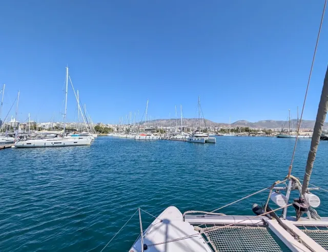 A view from a boat bow over a marina full of moored sailboats, and hills on the horizon