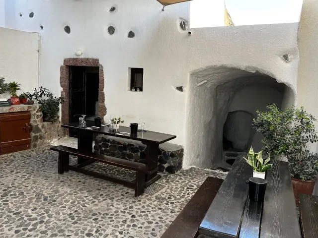 A whitewashed courtyard with pebble paving, dark wooden tables and an arched cave entrance