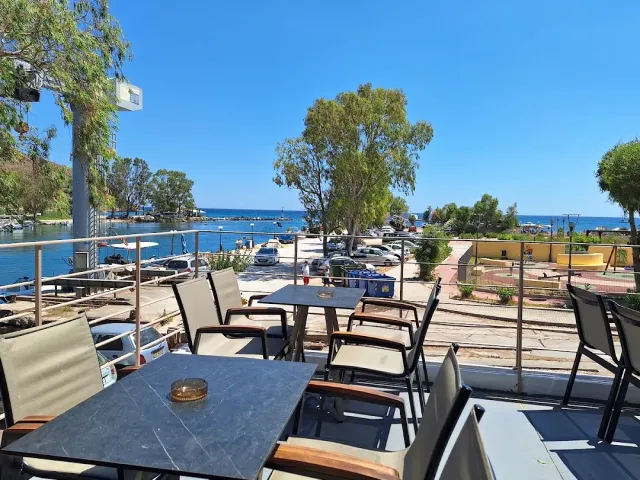 Grey tables on a balcony, with a small marina, trees and a blue sea behind