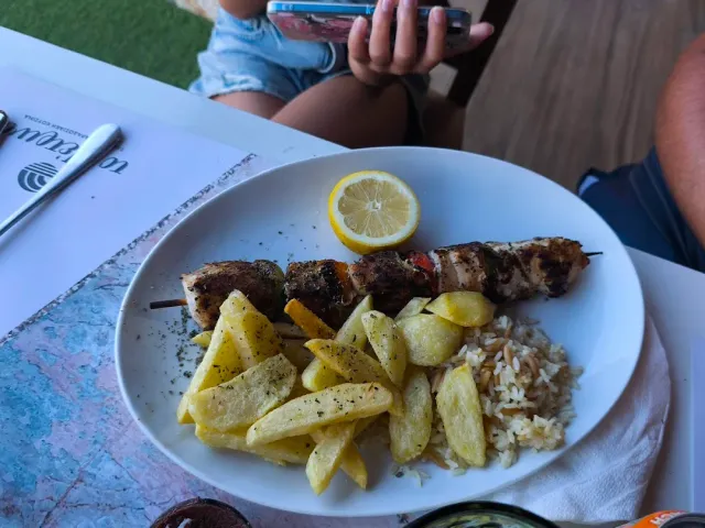 A plate with meat skewers, fried potatoes, rice and a lemon wedge