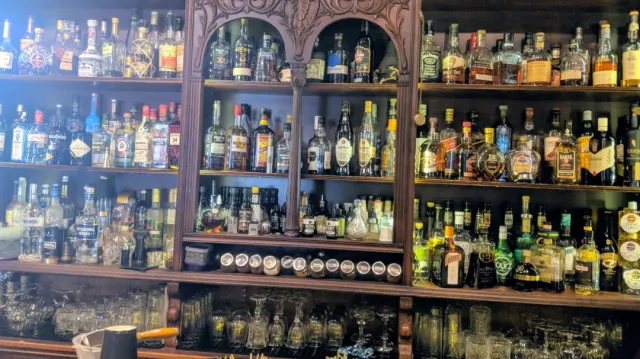 Carved wooden shelves loaded with hundreds of bottles, and glasses in rows at the bottom