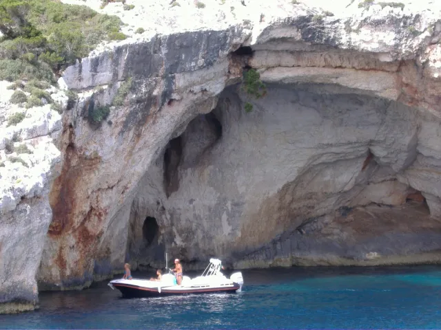 A small boat under white rock arches above bright blue water
