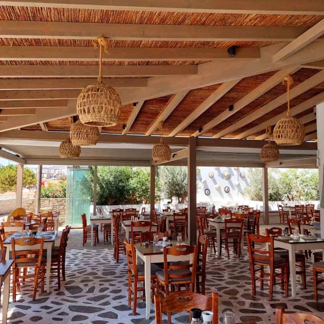 A reed roofed dining area with wicker lamps, reddish chairs and a pebble floor