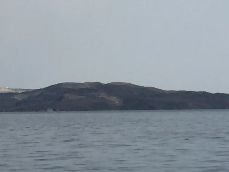 The black volcanic island of Nea Kameni above the Santorini caldera water on a grey hazy day