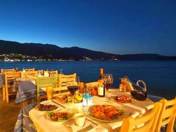 A table loaded with dishes and wine glasses at the water edge, after dark