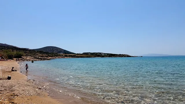 A wide sandy beach with clear shallow water, and low hills in the background