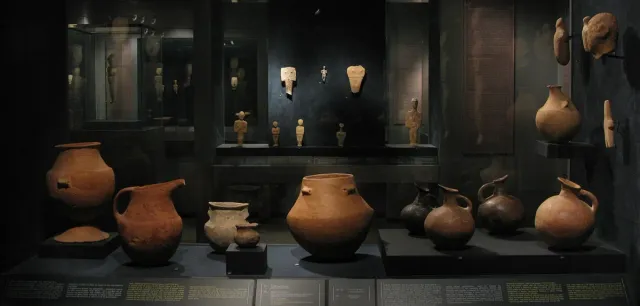 A display case with ancient clay vessels and lit marble figurines behind