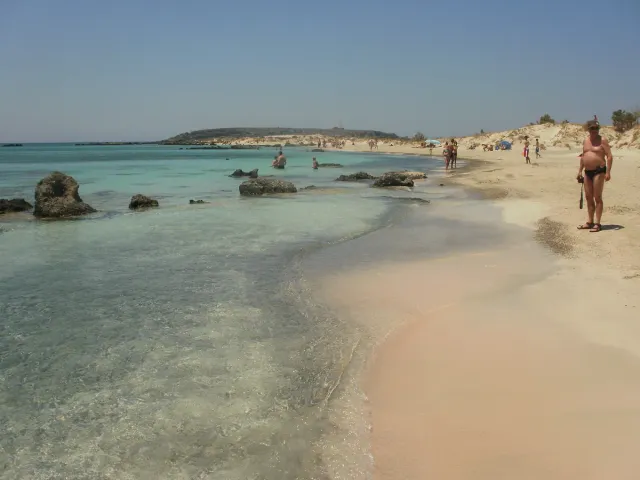 A strip of pinkish sand and shallow turquoise water with scattered rocks