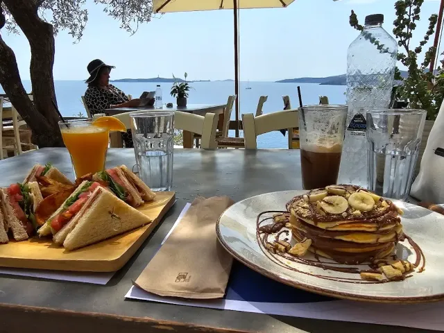 Triangular sandwiches, pancakes with banana and orange juice on a table facing the sea
