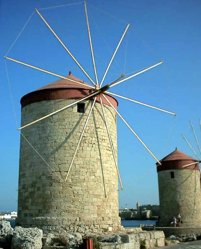 Round stone windmills with wooden sails, standing in a row on the pier