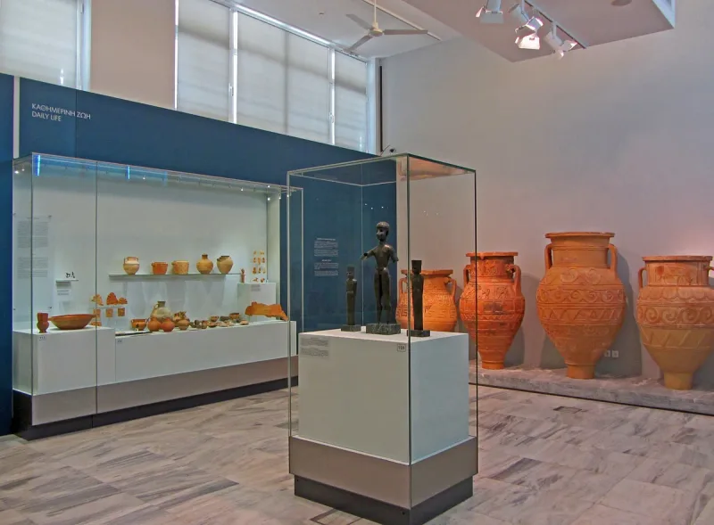 A gallery with glass display cases and giant clay storage jars behind