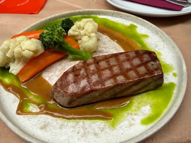 A grilled steak with grill marks, with steamed vegetables and two sauces