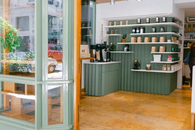 A green counter with shelves holding coffee bags and jars, beside a wooden window
